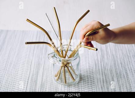 Child hand take golden metal drinking straw from glass jar in home kitchen. Sustainable lifestyle concept. Stock Photo