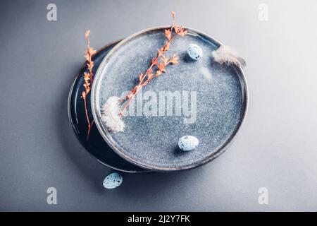 Easter preparation. Close up of dishes with eggs, feathers and spring branches. Ceramic plates on grey background. Stock Photo