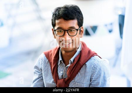 Portrait of a young Asian man wearing glasses standing outdoors with a sweater draped over his shoulders against a high key background Stock Photo