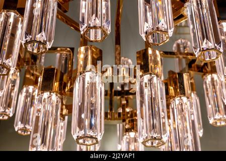 Close up on the stylish faceted glass prisms of a modern chandelier with gold or brass detail hanging from a ceiling in an interior decor concept Stock Photo