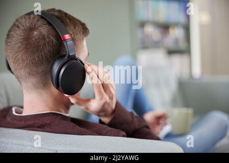 Close Up Of Man At Home Wearing Wireless Headphones Relaxing On Sofa Streaming Music OrListening To Podcast Stock Photo