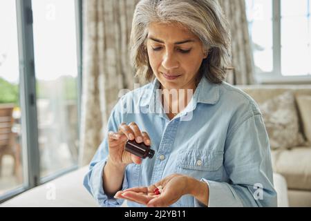 Mature Woman Sitting On Sofa At Home Taking Medication Stock Photo