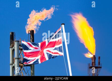 UK flag against refinery/gas processing plant chimneys. Cost of living crisis, rising gas, energy prices, global warming, Russian gas
