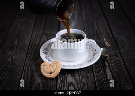 pouring black espresso coffee from coffee maker into white cup on wooden background Stock Photo