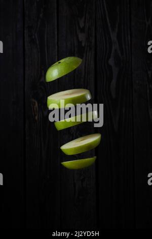 Levitation of a green apple cut into slices on a dark wooden background Stock Photo