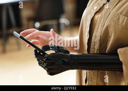 Close-up of girl with prosthetic arm adapting and learning to type a message on her mobile phone Stock Photo