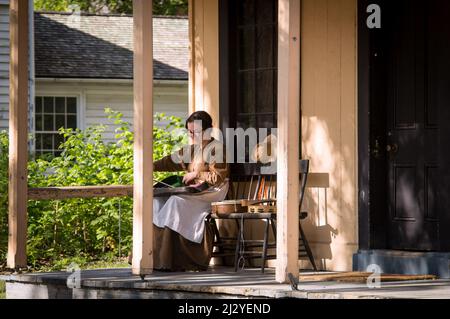 Toronto, Canada - 2019 08 24: A woman wearing 19th century style costume packs her violin into the case on the porch of the old wooden house in the op Stock Photo