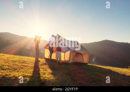 Group of friends pitching a tent on campground hill in the sunset at countryside Stock Photo