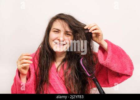 A woman in a pink robe combs her wet hair with a comb and laughs Stock Photo