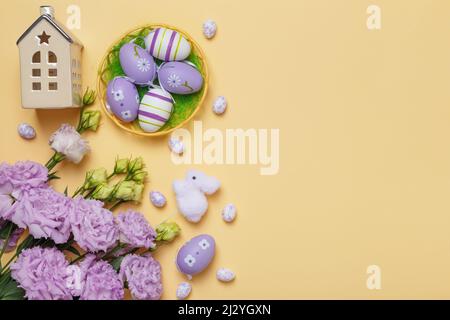 Easter card. Small toy house eggs in a basket bouquet of purple flowers on a yellow background with copy space. Stock Photo
