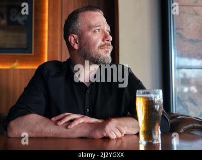 Hipster man sitting at the pub or bar table and drinking a glass of beer. Stock Photo