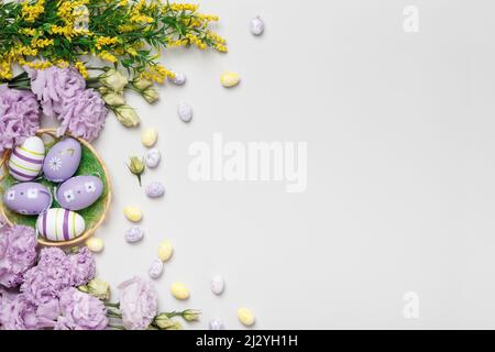 Easter greeting card. Purple flowers in blooming yellow twigs eggs in a basket on a gray background Stock Photo