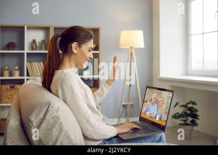 Happy woman talking to relatives using video call app on laptop sitting on sofa in her apartment. Stock Photo