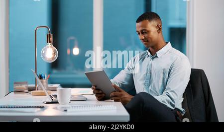 Keep yourself updated to all the latest business trends. Shot of a handsome young businessman using a digital tablet while working late in his office. Stock Photo