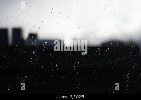 Blurred reflection of city silhouette in glass covered with raindrops Stock Photo