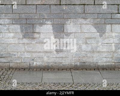 Wet gray stone wall made of rectangular blocks. The cobblestone sidewalk is in front of a facade. The building exterior is an abstract background. Stock Photo