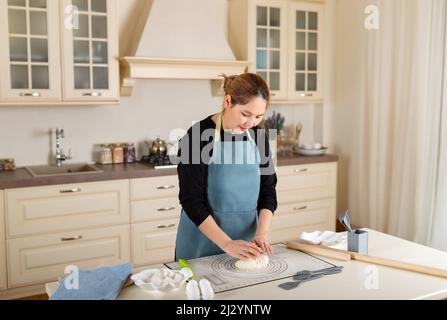 Young Central Asian woman cooking from dough in modern kitchen. Stock Photo