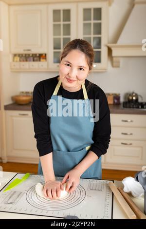 Young happy smiling kazakh woman portrait cooking from dough in modern kitchen, look at camera. Stock Photo