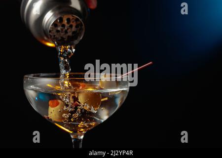 Martini with green olives. The cocktail is poured from a shaker into a glass. Stock Photo