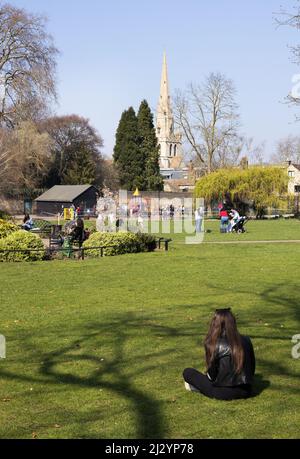 Woman in park; Woman sitting in a park on a sunny spring day, Christ's Pieces park, Cambridge City Centre, Cambridge  UK Stock Photo