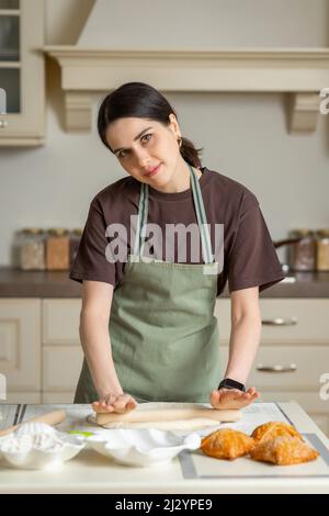 Cute young brunette woman in a kitchen apron is cooking in the kitchen. Stock Photo