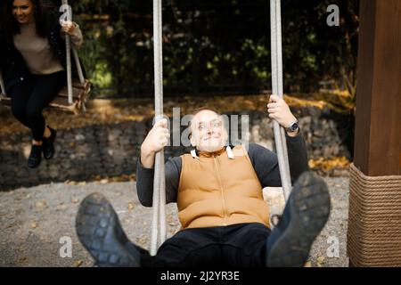 Young man having fun with his beloved swinging on a swing with high legs outdoor. High quality photo Stock Photo