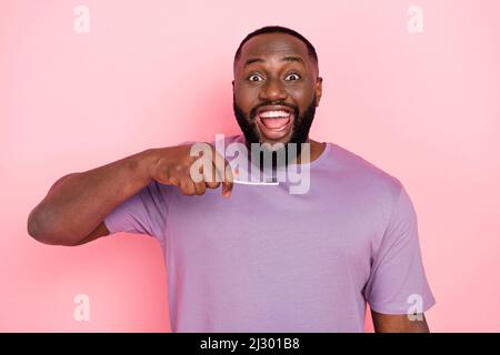 Photo of impressed funny guy dressed violet t-shirt cleaning teeth isolated pink color background Stock Photo