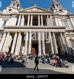 London, Greater London, England,  March 12 2022: Tourists sitting on the steps outside the entrance to St Pauls Cathedral. Lady wearing a mask stands Stock Photo