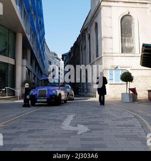 London, Greater London, England,  March 19 2022: Man in silhouette walks past a blue taxi in the City of London. Road Sign in foreground. Stock Photo