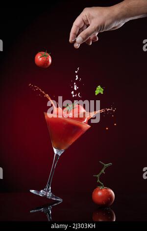 Tomato fall down in tomato juice with explosion and spashing of tomato juice on dark red background. Juice Levitation concept. Stock Photo