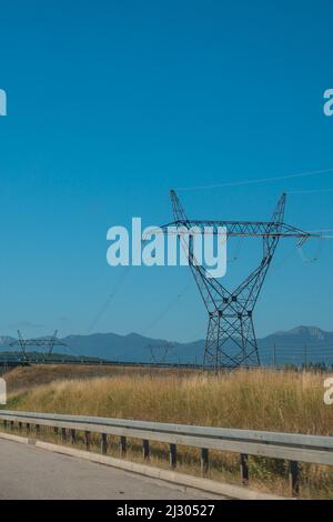 High voltage pole with blue sky, blue sky, trees and grass. Stock Photo