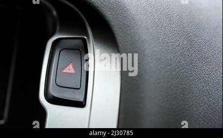 Red warning light triangle button in modern car interior panel, closeup detail Stock Photo