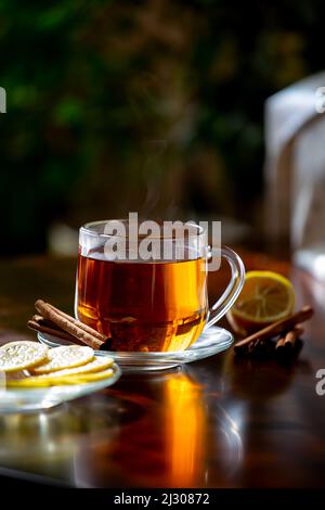 A cup of hot freshly brewed tea with lemon and cinnamon in the sun on a dark wooden background Stock Photo