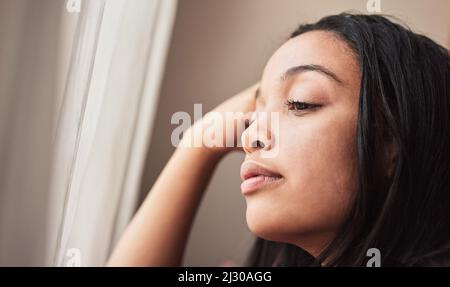 I wonder what everyone is up to. Shot of young woman looking thoughtful at home. Stock Photo