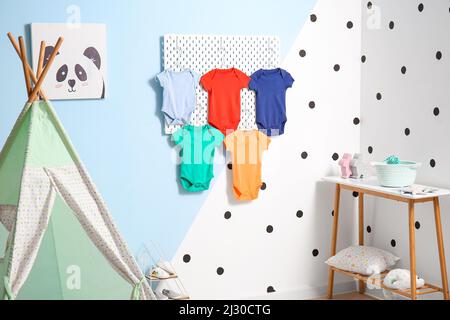 Pegboard with baby bodysuits hanging on color wall in children's room Stock Photo