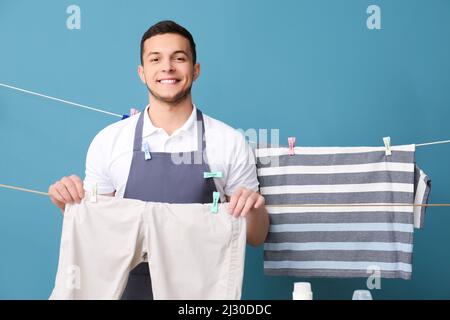 Young man with hanging clean laundry and clothespins on blue background Stock Photo