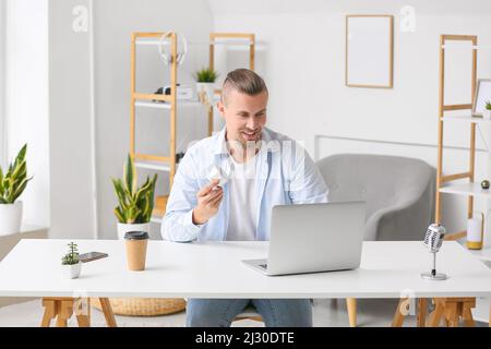 Man holding wireless portable speaker and using laptop at table in light room Stock Photo