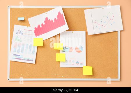 Board with blank sticky notes and charts hanging on beige wall Stock Photo