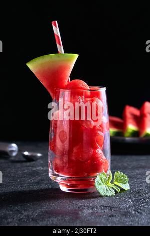 Ripe watermelon noisette balls in glass with mint on dark background. Summer dessert Stock Photo