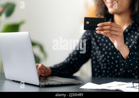 Online shopping. Close-up of dark skinned female hand holds credit card. Woman pay for purchases and deliveries on the Internet, enter card details to pay for good, contactless payment Stock Photo