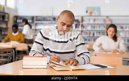 Focused adult latin american student studying in library Stock Photo