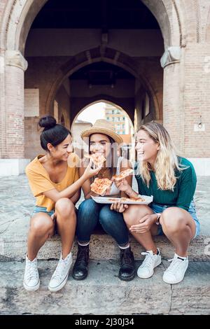 Happy multiracial women eating pizza in city street Stock Photo