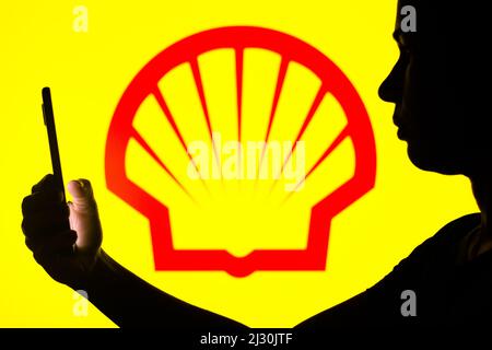 In this photo illustration, a woman's silhouette holds a smartphone with the Shell logo in the background. Stock Photo