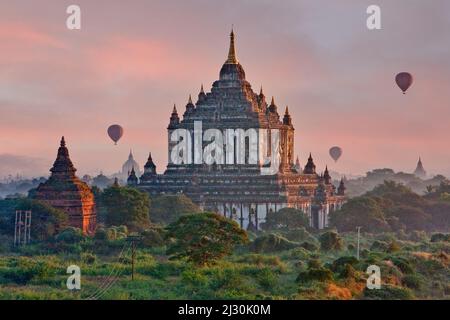 Myanmar, Burma, Bagan.  Hot-air Balloons Begin to Rise over Thatbyinnyu Temple, Early Morning. Stock Photo