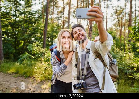 Young couple taking selfie picture with smartphone while hiking in the woods Stock Photo