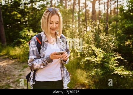 Young woman using mobile phone while walking in the woods during summer hike Stock Photo