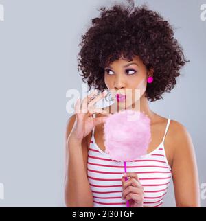 Candid candy floss. Studio shot of a beautiful young woman against a gray background. Stock Photo