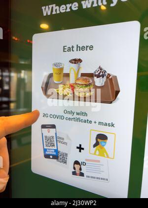 Basel, Switzerland - Dec 20, 2021: Male hand touching order kiosk inside McDonald's restaurant in central Basel - special instruction to eat only with 2G covid certificate and respiratory mask Stock Photo