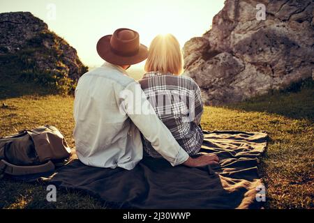 Rear view of young couple sitting on blanket in the mountains enjoying a beautiful sunset together Stock Photo