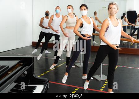 Group of men and women in protective masks practicing at ballet barre Stock Photo